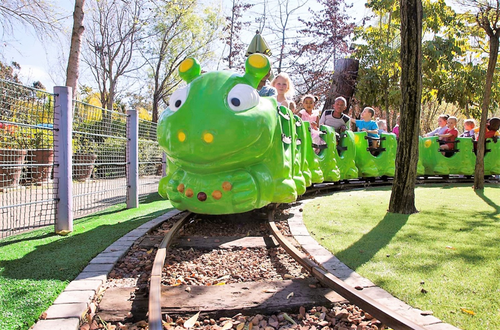 A big green train shaped like a catipillar full of children coming toward the camera.  It is all bright and fun and showing what Bugz Playpark has to offer.