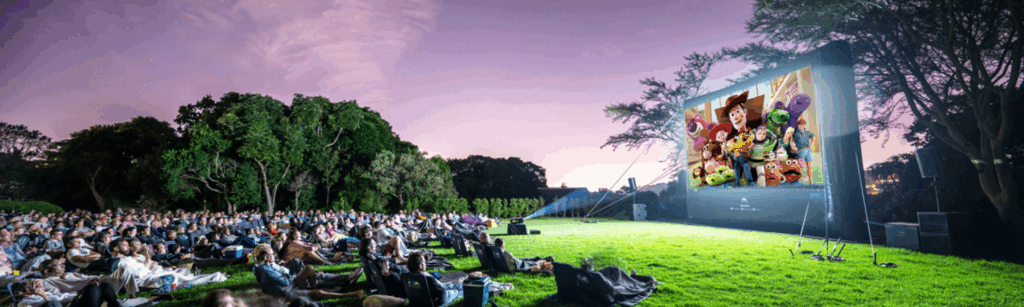 A large crowd watching an outdoor movie at The Galileo Open Air Cinema in Kirstenbosch Gardens with mountain views at sunset.