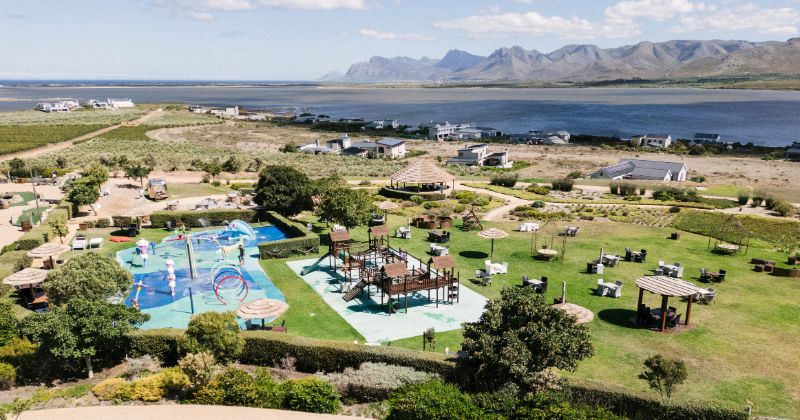 Aerial view of Benguela Cove Wine Estate, showcasing the outdoor play area, water play zone, and stunning scenic surroundings with mountains and vineyards.