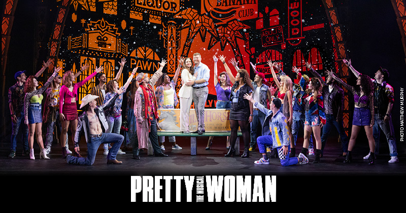 A vibrant scene from Pretty Woman: The Musical featuring a large cast of performers on stage, with a neon-lit backdrop of a city street. The central characters, Vivian Ward and Edward Lewis, are surrounded by the ensemble cast, all striking dynamic poses. The Pretty Woman logo is displayed at the bottom of the image.