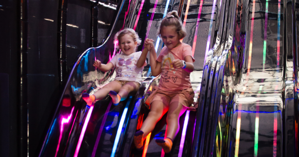 Children having fun at Playrock Adventure Park Cape Town, sliding down brightly lit, multi-colored slides.