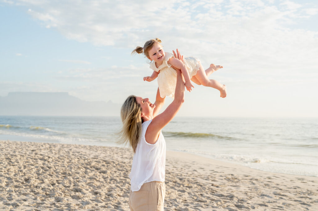 Mother lifting her young daughter on the beach during a joyful family photo session by Chasing Light Photography.